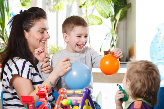 woman with two children playing with balloons in home interior