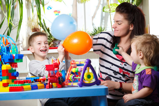 woman with two children playing with balloons in home interior