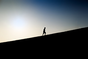 Fototapeta premium Silhouette of a man climbing a hill