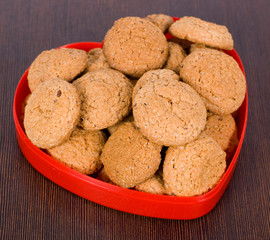 Oatmeal cookies in a red heart plate on a brown surface