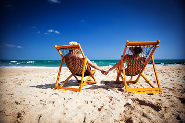 Couple sitting in beach chairs and holding hands on a tropical b