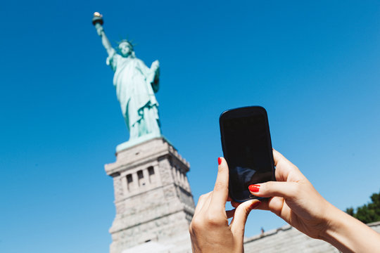 Woman takes a photo of Statue of Liberty with cell phone