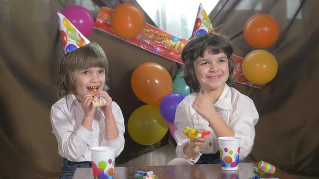 Young beautiful twin girls blowing party horns 