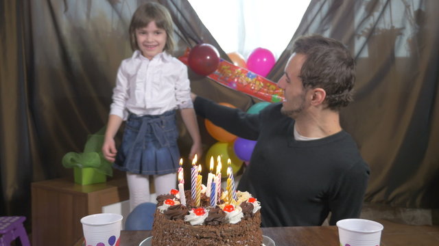 Man blowing candles on a birthday cake with his daughter