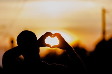 Sunset. Silhouette hand in heart shape with sunrise in the