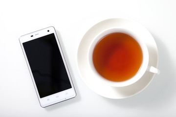 White smartphone and a cup of tea on white glass table