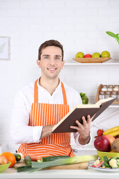 Man with recipe book in hands at table with different products