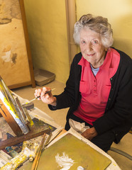 Senior woman painting at her easel, in her studio in France.
