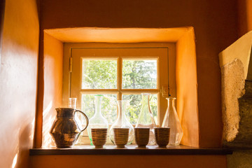 Small window with bottles, jug and cups in an old stone house