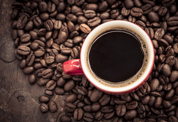 Red cup filled with hot coffee on top of roasted coffee beans