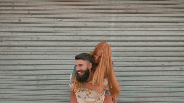 Redhead girl laughing loudly while hipster boyfriend piggyback