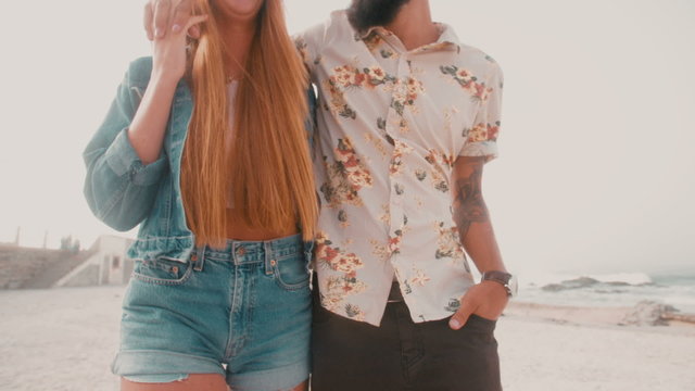 Hipster couple walking together arm in arm on a beach
