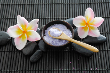Set of stones with frangipani with salt in bowl ,spoon on mat


