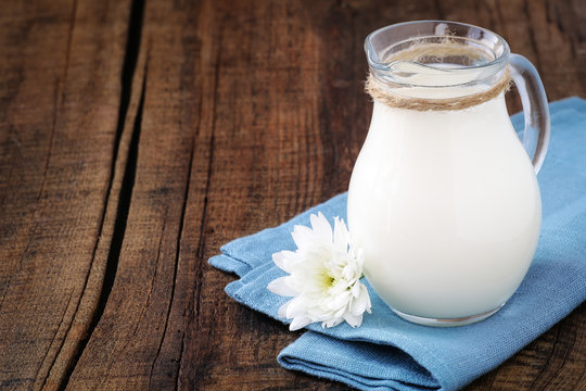 Fresh milk in a glass jug on a blue napkin with a flower