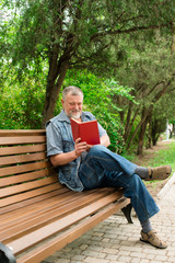 old man reading a book on a park bench