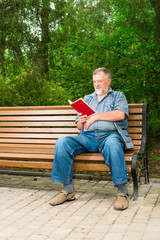 Fototapeta premium old man reading a book on a park bench