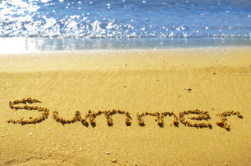 Summer written in the sand on beach with blue waves
