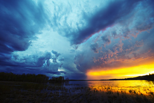 Sunset on the horizon over a lake, and storm clouds rising.