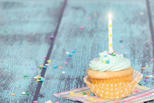 Pastel cupcake with a candle on vintage background