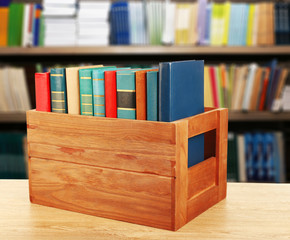 Books in wooden crate on bookshelves background