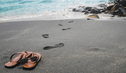 Fototapeta na wymiar Human leave his flip flops on the black sandy beach and go to sw