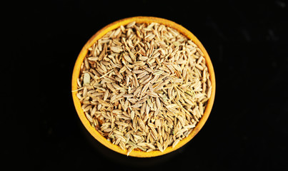 Cumin in wooden bowl, isolated on black