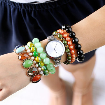 Stylish bracelets and clock on female hand close up