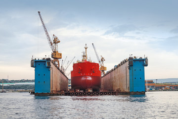 Floating blue dry dock with red tanker under repair