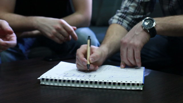 Hands of young people who draw a draft with pen on notebook