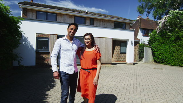 Portrait of happy asian couple standing in front of their home on a sunny day