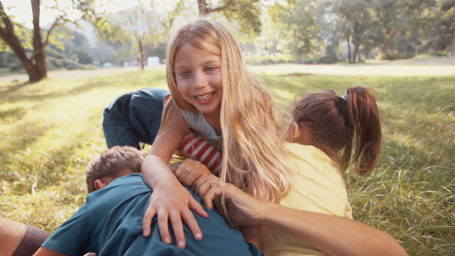 Children climbing and tickling father lying in grass in park