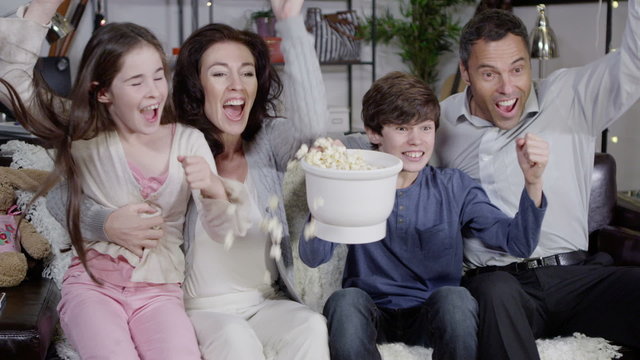 Happy family watching sports on t.v. and spilling popcorn everywhere
