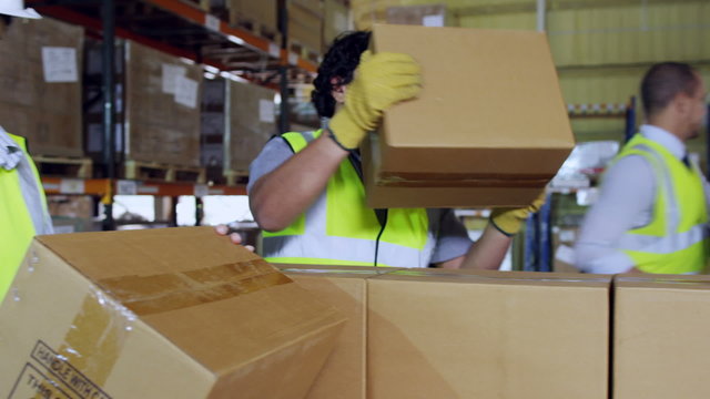 Warehouse workers in high visibility clothing taking brown boxes from a pallet