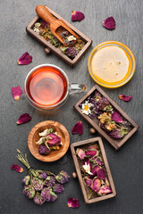 Herbal tea with honey, dried herbs and flowers on black stone