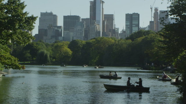 People in rowboats on central park lake with the New York skyline behind them