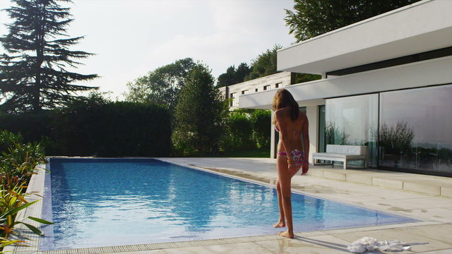 Beautiful woman outside modern home slips out of her robe for a swim in the pool