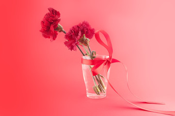 Three red carnations in vase with ribbon on a red background.