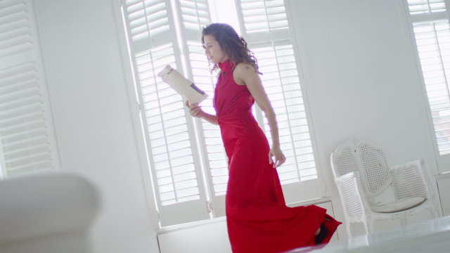 Beautiful woman in evening gown returns home and takes off her shoes