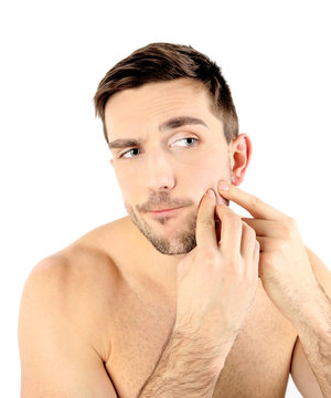 Handsome young man squeezing pimple isolated on white