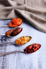 Dried fruits in silver spoons on color wooden table background