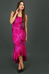 Beautiful young woman in long pink dress on dark gray