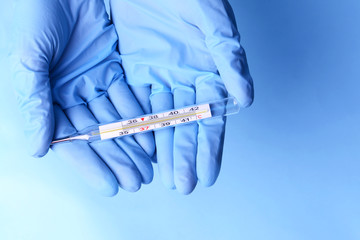 Hands with gloves holding thermometer on blue background
