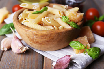 Raw pasta in bowl with cheese and vegetables on table close up