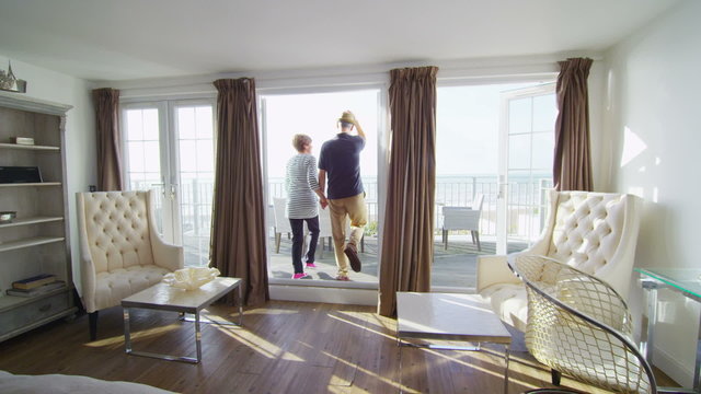 Romantic couple go to look at the view from balcony of their beachside apartment
