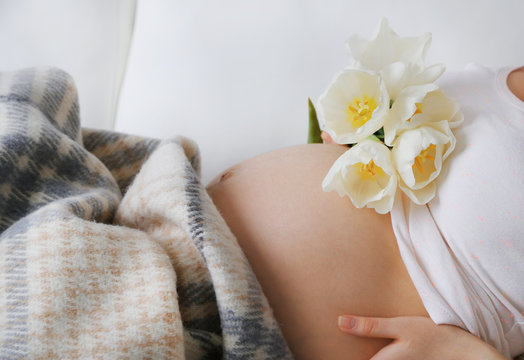Young pregnant woman lying on sofa with flowers close up