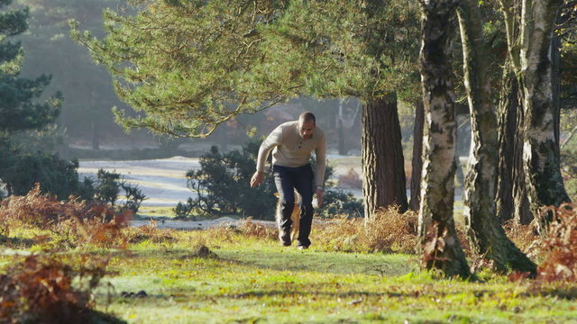 A handsome man running with his dog through the forest