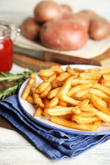 Tasty french fries on plate, on wooden table background