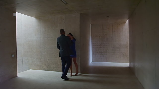 Sexy young couple walking through modern concrete building stop to share a kiss