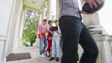 Happy group of students using tablet computer outside elegant college building