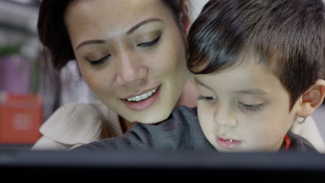 A mother teaches her young son how to use a computer